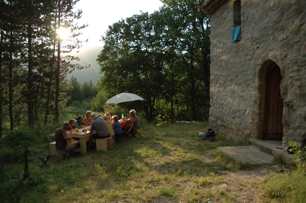 Groupe partageant un repas en plein air devant le Refuge d'Art La Forest d'Andy Goldsworthy au coucher du soleil - Ambiance conviviale séjour randonnée Haute-Provence