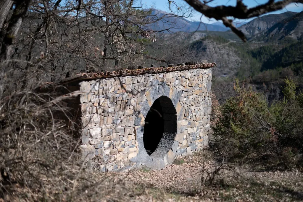 Andy Goldsworthy's Refuge d'Art des Bains Thermaux, a dry-stone shelter pierced by a single oval opening, the mountains of Haute-Provence behind