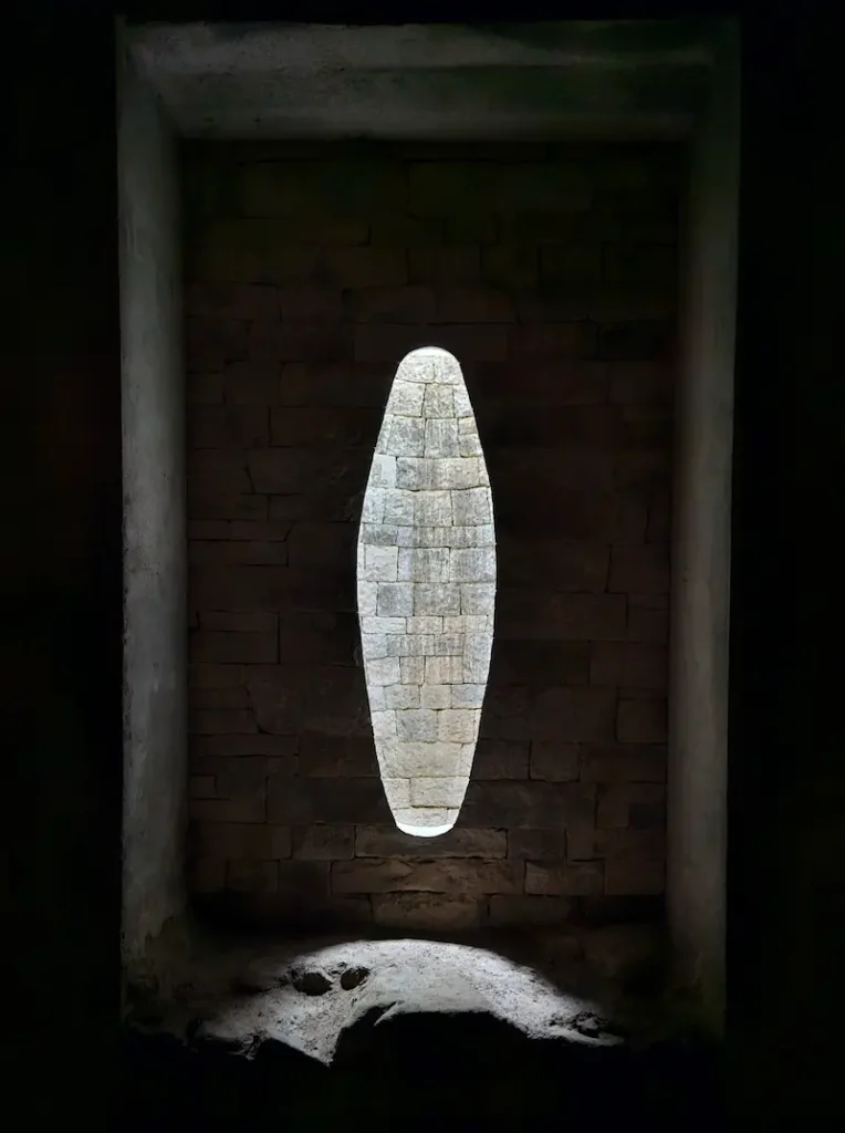 Pale limestone ovoid set into the dark stone wall inside Andy Goldsworthy's Refuge d'Art La Forest, lit from within, Haute-Provence